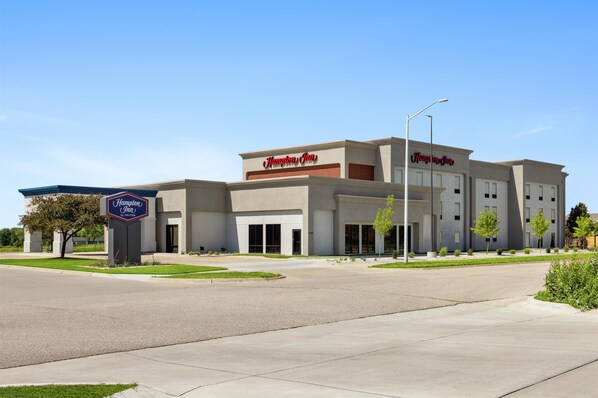 A Hampton Inn hotel with a modern design, featuring a large sign, multiple windows, and a well-maintained lawn.