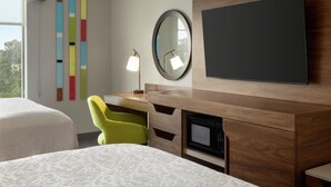 A hotel room with a bed, a desk with a chair, a flat-screen TV, a microwave, and a mirror.