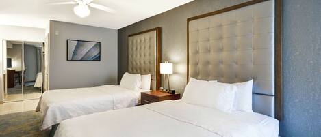 A hotel room with two beds, a ceiling fan, a bedside table with a lamp, and a framed picture on the wall.