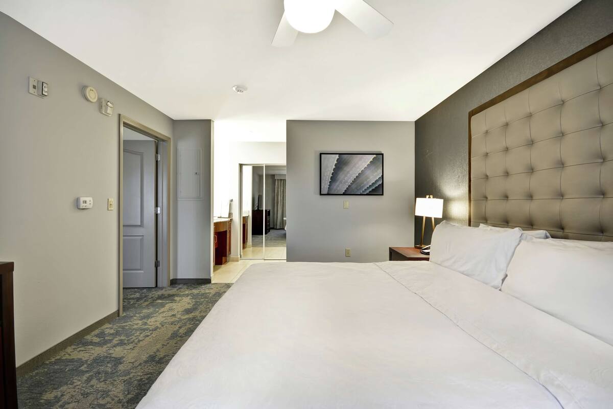 Een hotelkamer met een groot bed, een hoofdbord, een nachtkastje met een lamp en een deur naar een badkamer.