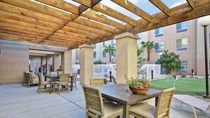 An outdoor patio area with a wooden pergola, a dining table with chairs, and a potted plant. - Homewood Suites by Hilton Palm Desert (Palm Desert)