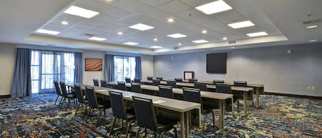A conference room with multiple tables and chairs, large windows with curtains, and a patterned carpet.