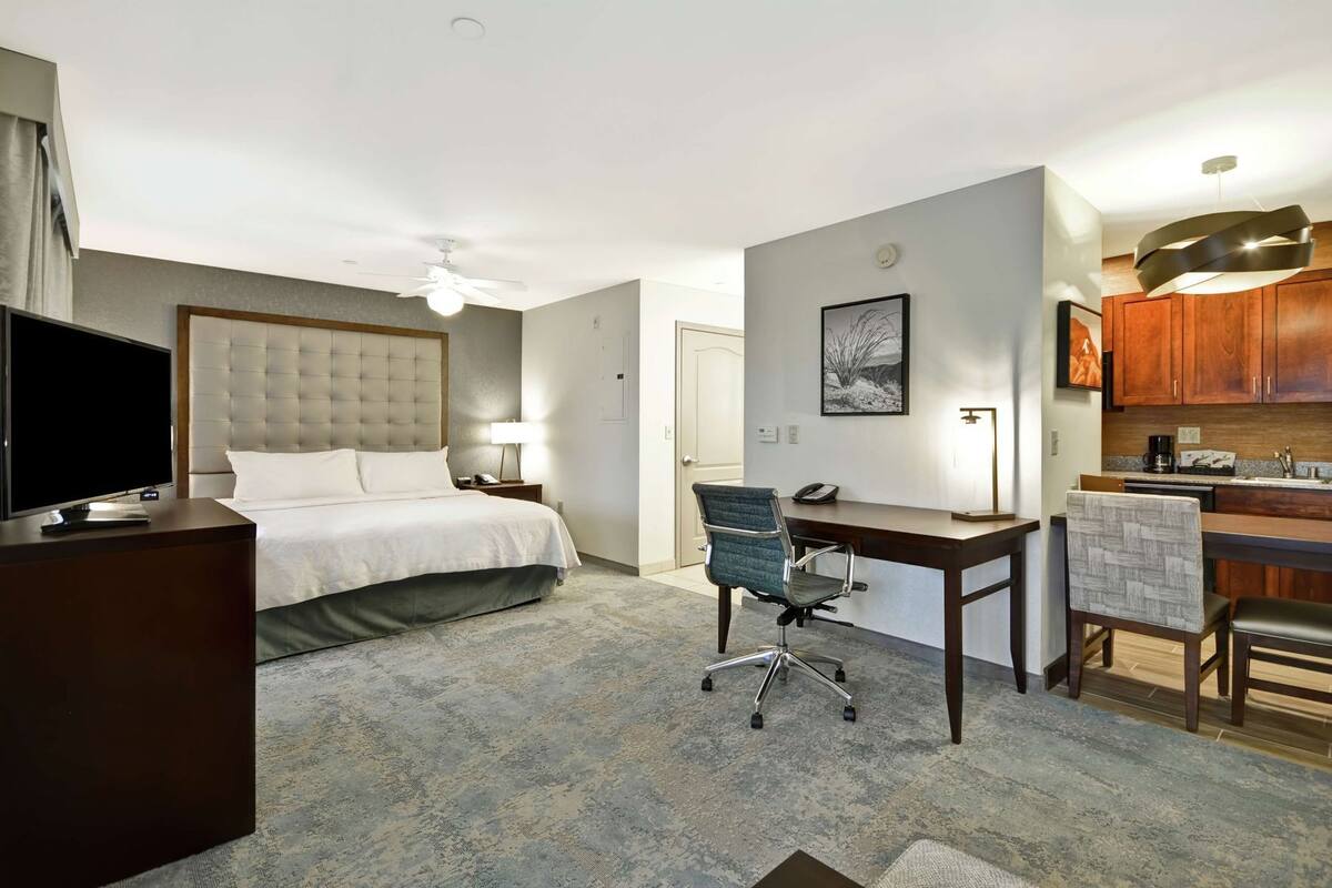 Habitación de hotel con cama, escritorio, silla, televisor y kitchenette.