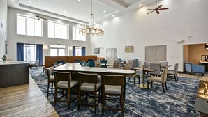 A spacious hotel lobby with a central round table, multiple seating areas, and a large window providing natural light. - Homewood Suites by Hilton Palm Desert (Palm Desert)