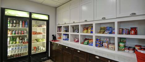 A kitchen with a white countertop, wooden cabinets, and a refrigerator stocked with beverages and snacks.