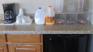 A kitchen counter with a coffee maker, salt and pepper shakers, milk jugs, a juice container, and a microwave. - Budgetel Inn and Suites (Rockingham)