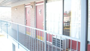 A building with a red door and a number 53 sign, a balcony with a metal railing, and a brick wall. - Budgetel Inn and Suites (Rockingham)