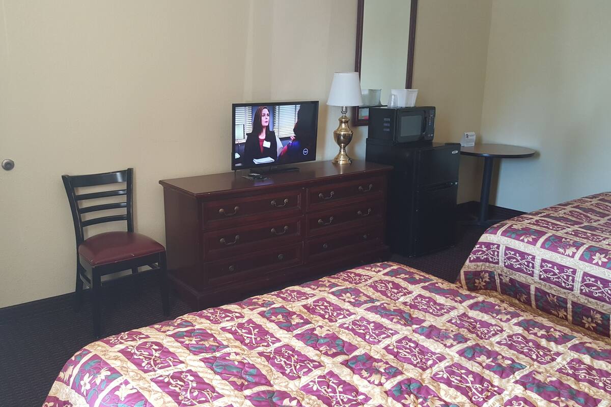 A hotel room with a bed, a TV on a dresser, a chair, a desk, and a lamp.
