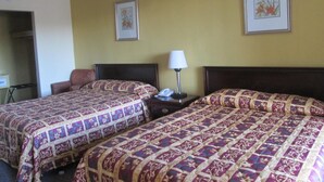A hotel room with two beds, each with patterned bedding, a bedside table with a lamp, and a wall clock.