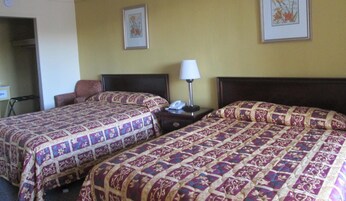 Habitación de hotel con dos camas, cada una con ropa de cama estampada, una mesita de noche con lámpara y un reloj de pared.
