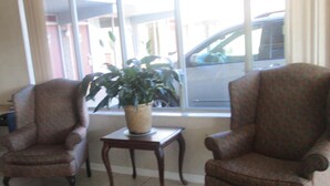A room with two patterned armchairs, a small wooden table, and a potted plant. - Budgetel Inn and Suites (Rockingham)