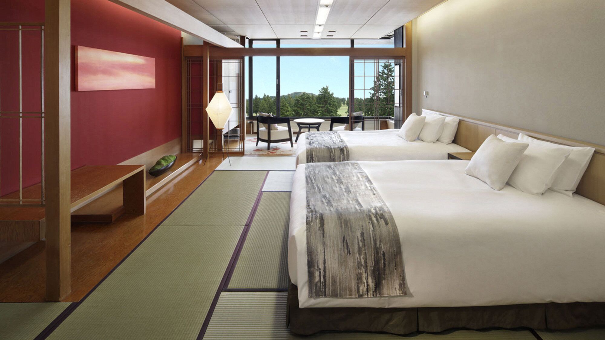 A hotel room with two beds, a view of trees, a dining area, and a red wall.