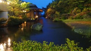 Edificio japonés tradicional con fachada de madera y un corredor cubierto a lo largo de un río tranquilo.