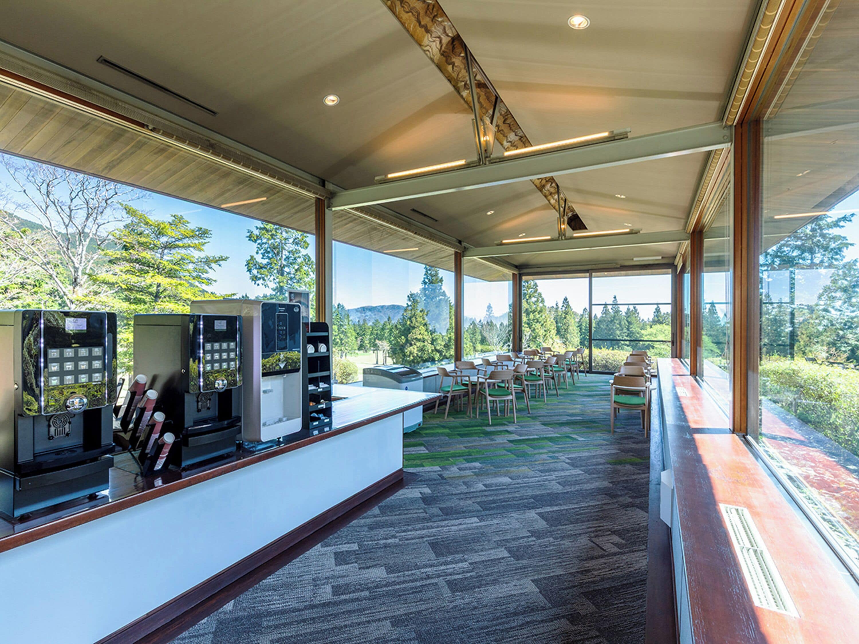 A modern indoor space with a reception desk, seating area, and large windows offering a view of greenery and hills.