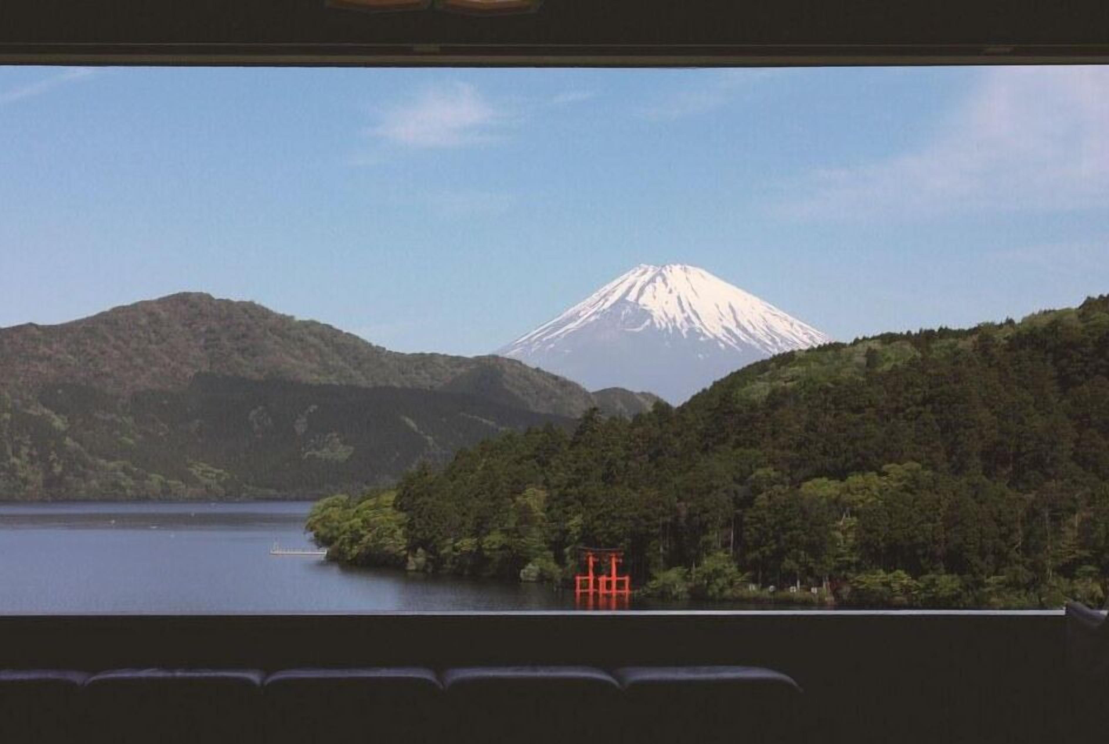 A view of a mountain with a snow-capped peak, a body of water, and a red structure in the foreground.