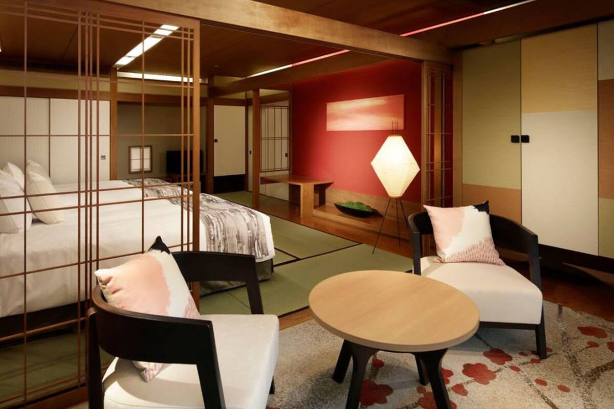 A hotel room with a bed, two chairs, a small table, a floor lamp, and a traditional Japanese sliding door.
