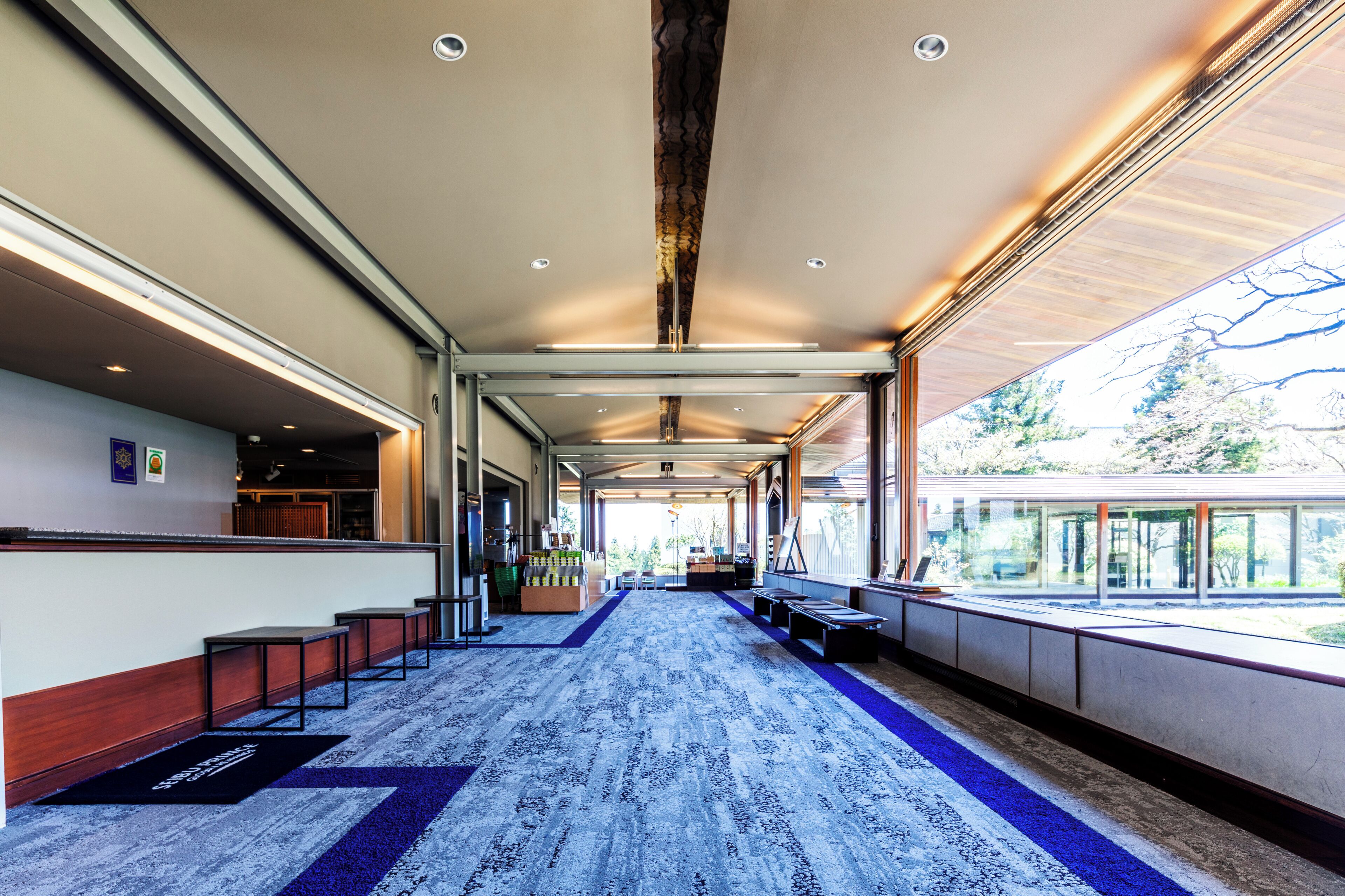 A hotel lobby with a long reception desk, seating area, and large windows offering a view of the outdoors.