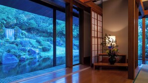 Un interior japonés tradicional con puertas correderas, suelo de madera y vista a una cascada a través de amplios ventanales.