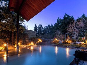 Un área de piscina exterior tranquila con un porche de madera, rodeada de abundante vegetación e iluminada con luces ambientales.