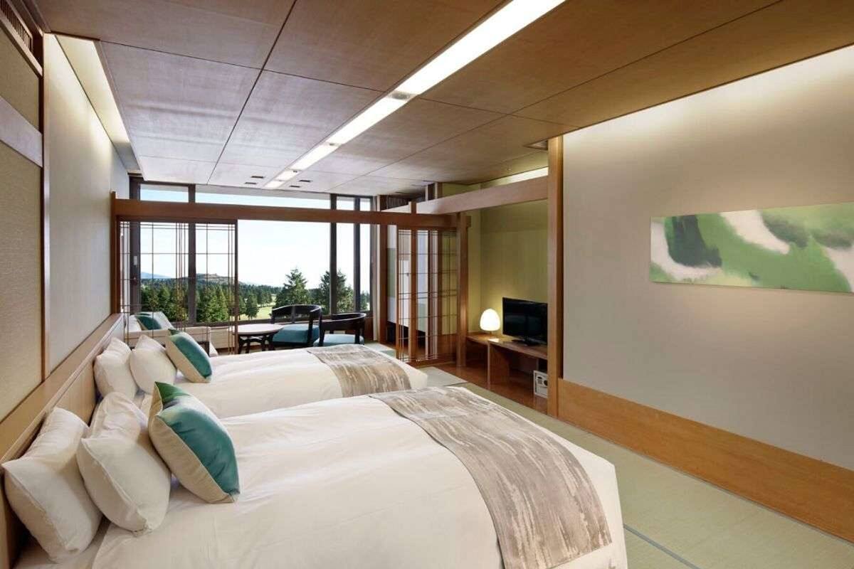 A hotel room with two beds, a television, and a large window offering a view of the outdoors.