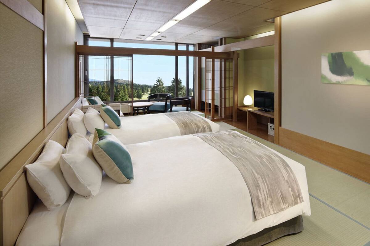 A hotel room with two beds, a TV, a desk, and a view of the outdoors.