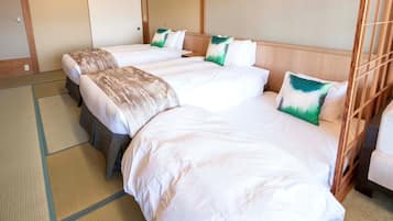 Una habitación de hotel con tres camas, cada una con ropa de cama blanca y almohadas verdes y blancas. La habitación presenta una estética japonesa tradicional con suelo de tatami y cabeceros de madera.