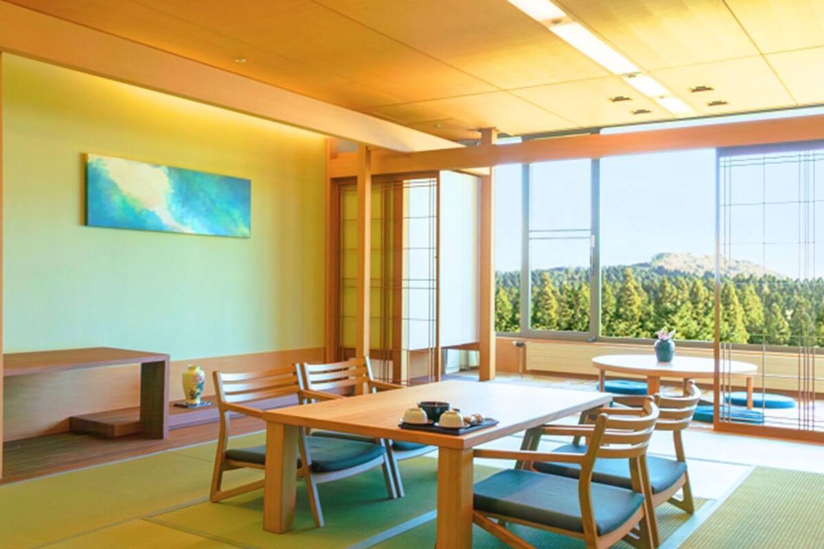 A traditional Japanese-style room with tatami flooring, a low table, and a view of a forested mountain.