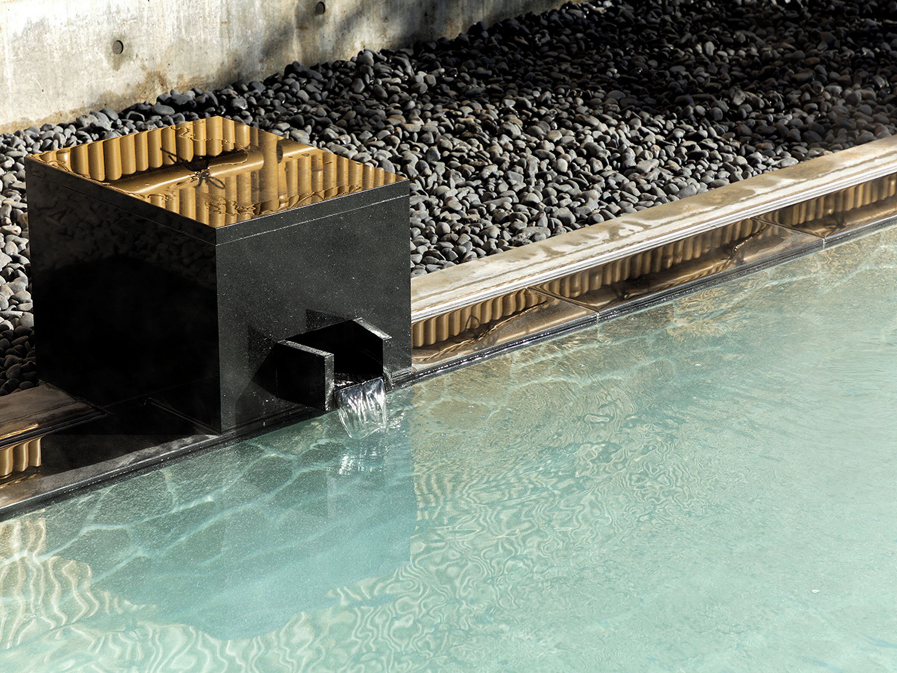 Une piscine à l’eau claire, bordée de galets et entourée d’une structure noire dotée d’une sortie d’évacuation.