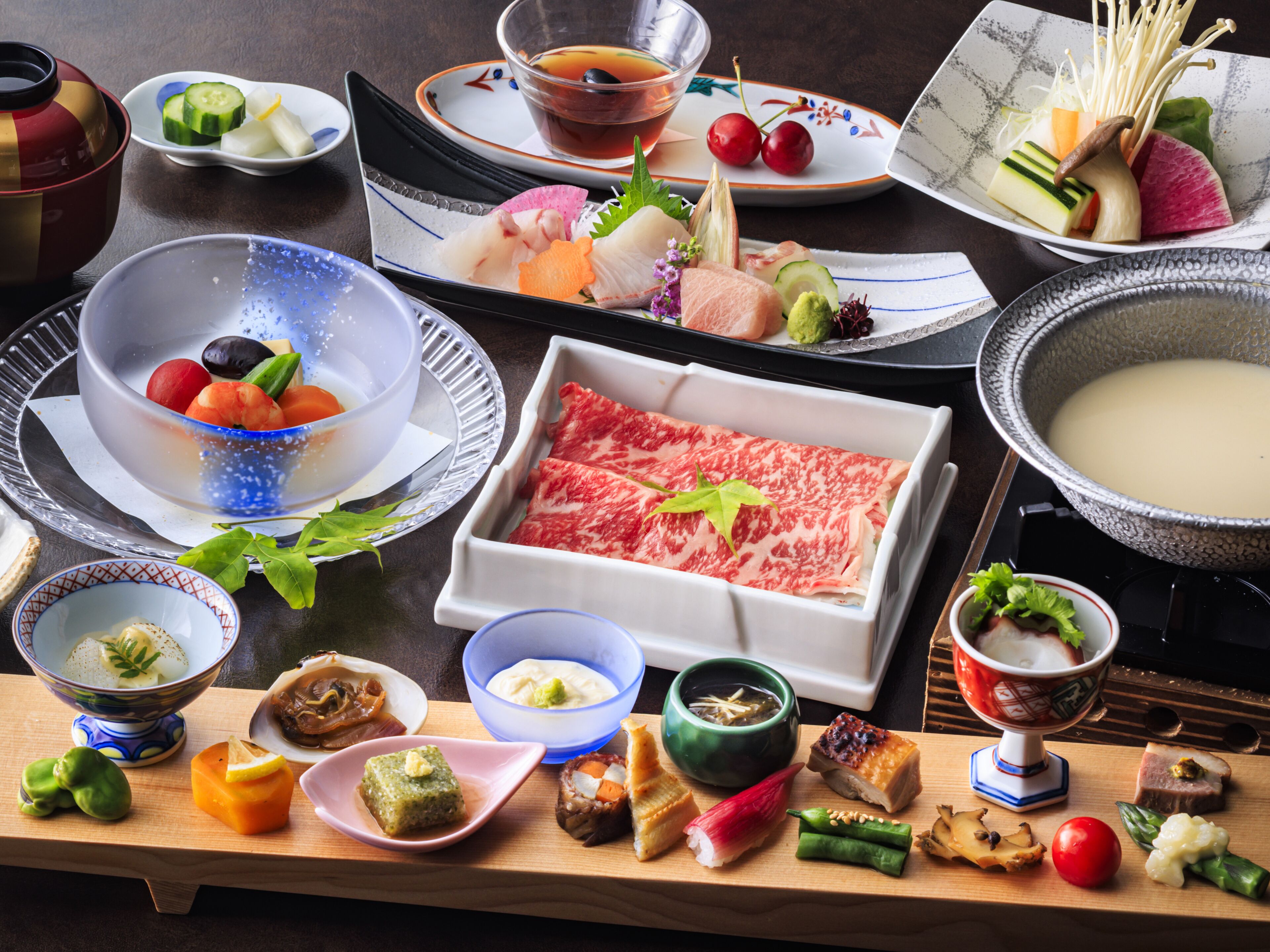 A variety of Japanese dishes including sushi, sashimi, and a hot pot, arranged on a wooden table.