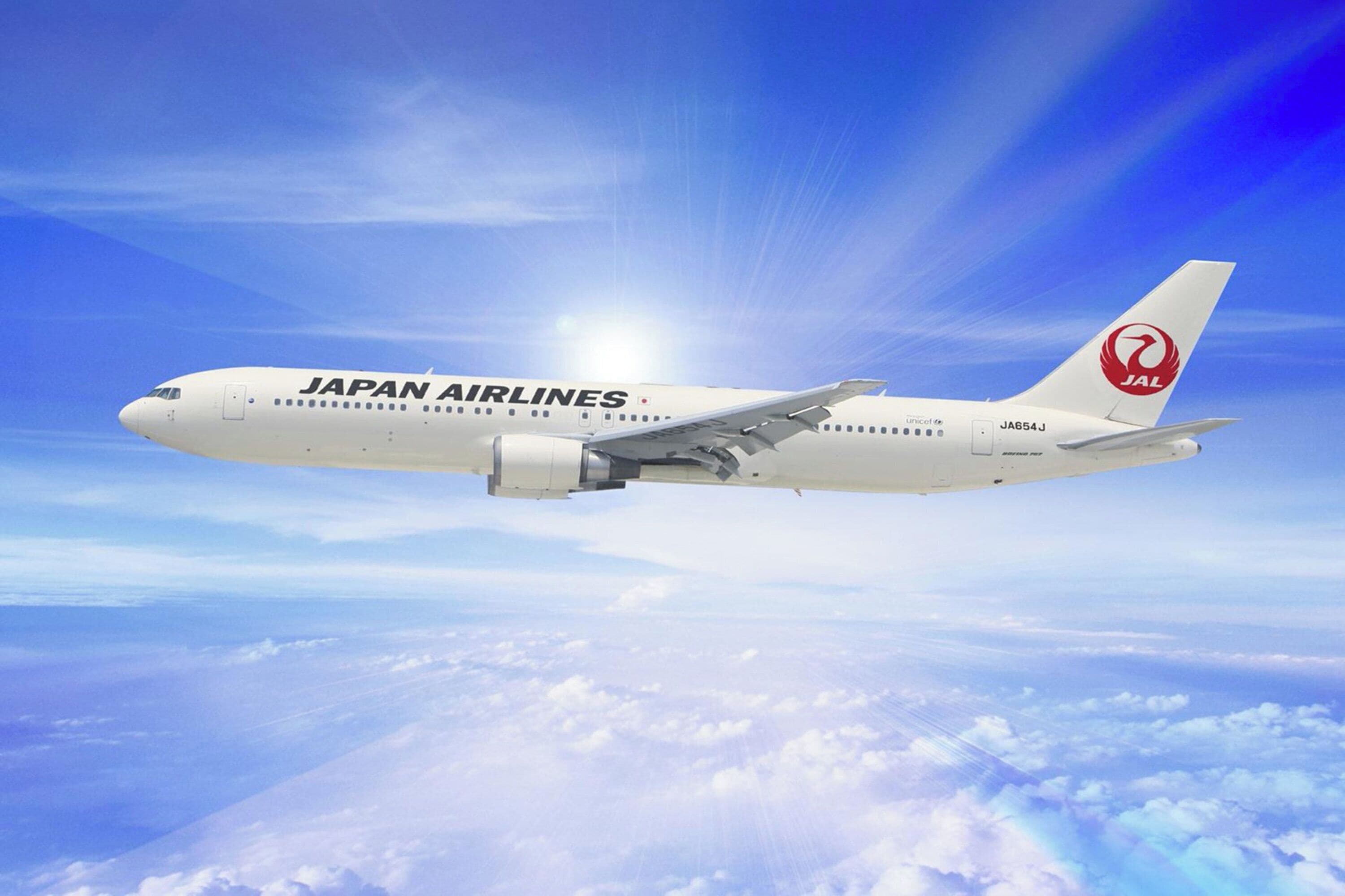 A Japan Airlines airplane in flight with a clear sky and clouds below.
