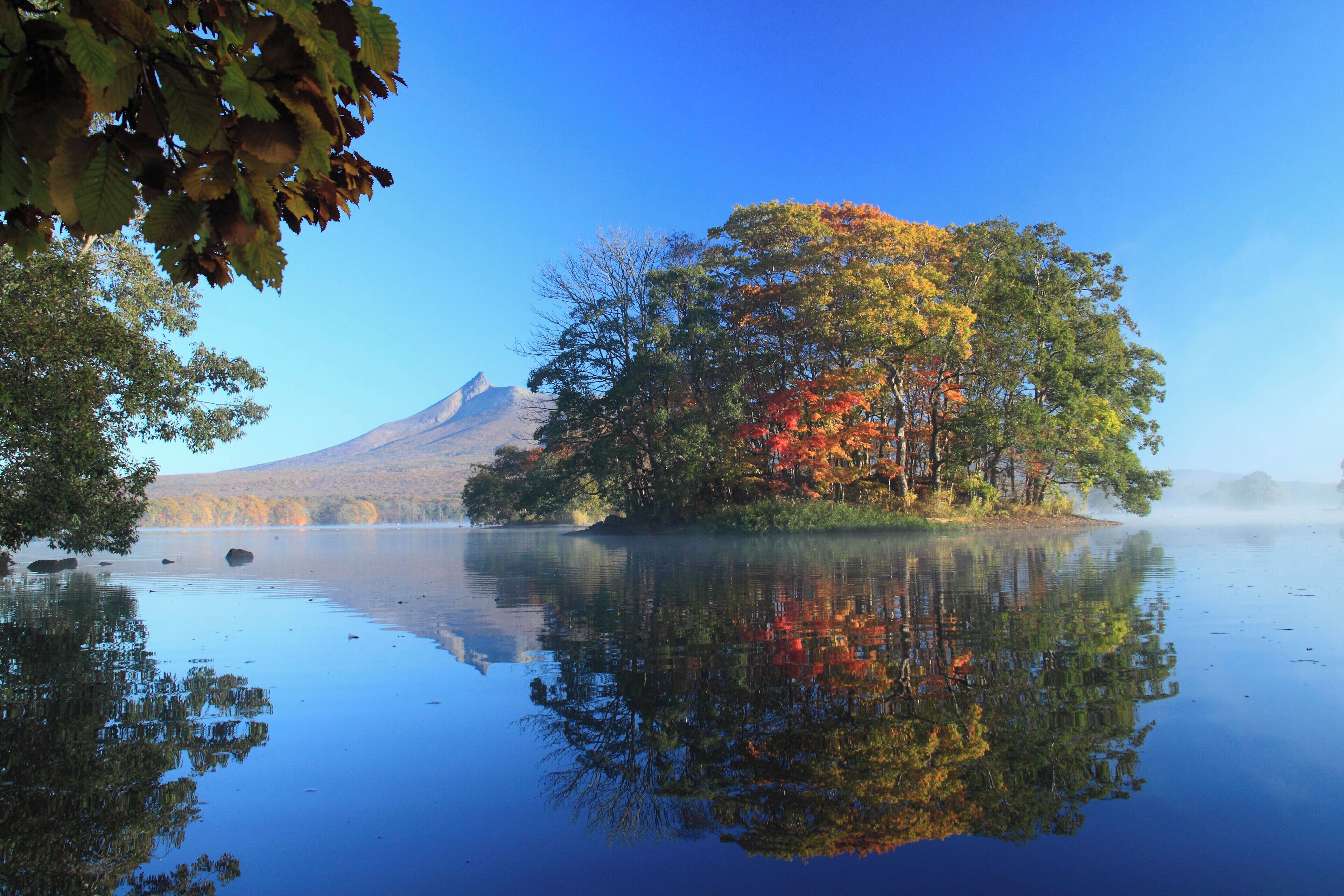 A calm lake with a reflection of trees and a mountain in the background.