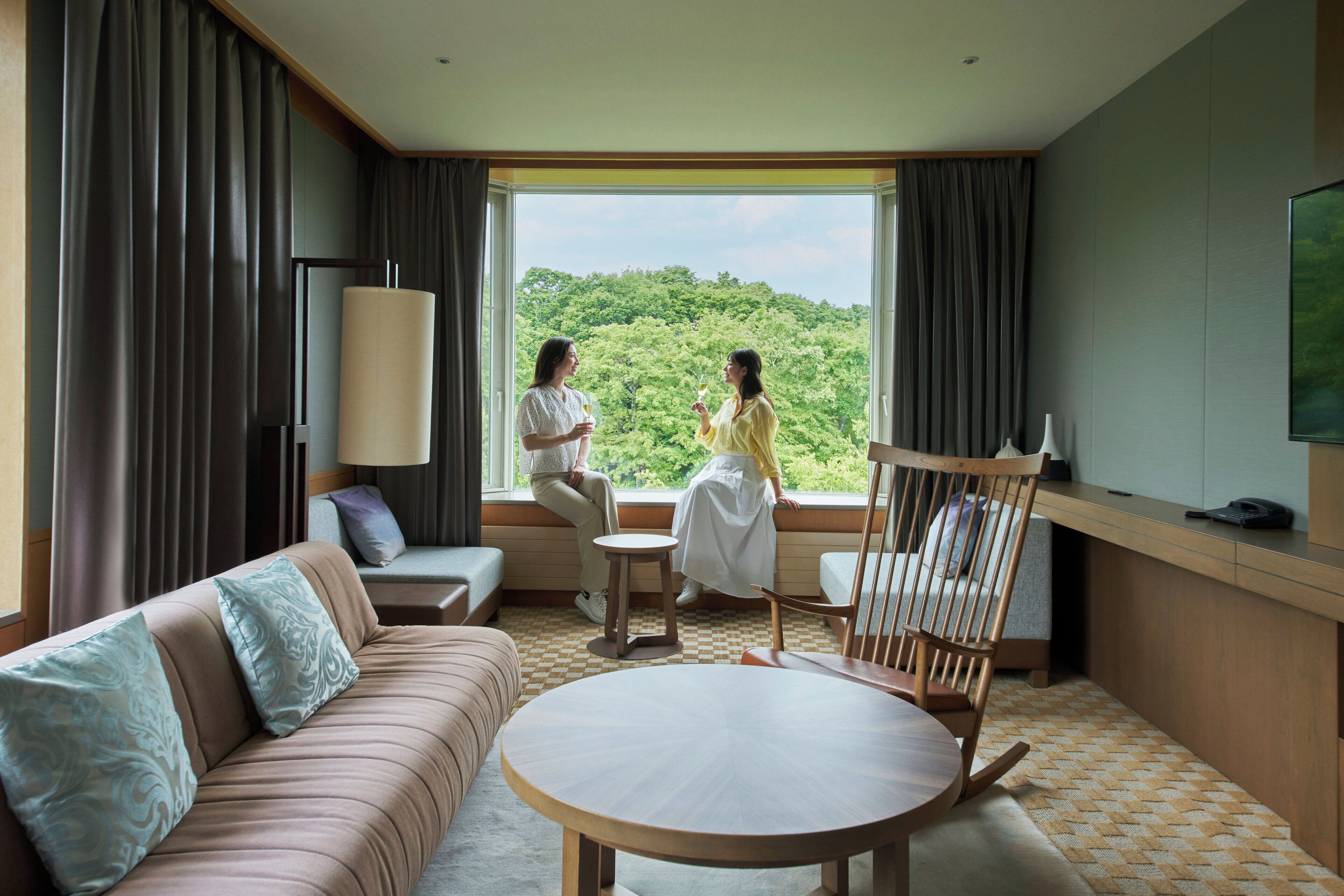 Habitación de hotel con un ventanal grande, un sofá, una mesa redonda y una silla.