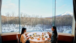 Two people dining at a round table with a view of a snowy forest and a mountain. - Hakodate Onuma Prince Hotel (Nanae)