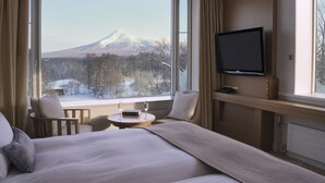 A hotel room with a bed, a TV, a small table with glasses, and a view of a mountain. - Hakodate Onuma Prince Hotel (Nanae)