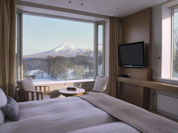 A hotel room with a bed, a TV, a small table with glasses, and a view of a mountain. - Hakodate Onuma Prince Hotel (Nanae)