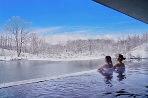 A couple in a heated outdoor pool with a snowy landscape and trees in the background. - Hakodate Onuma Prince Hotel (Nanae)