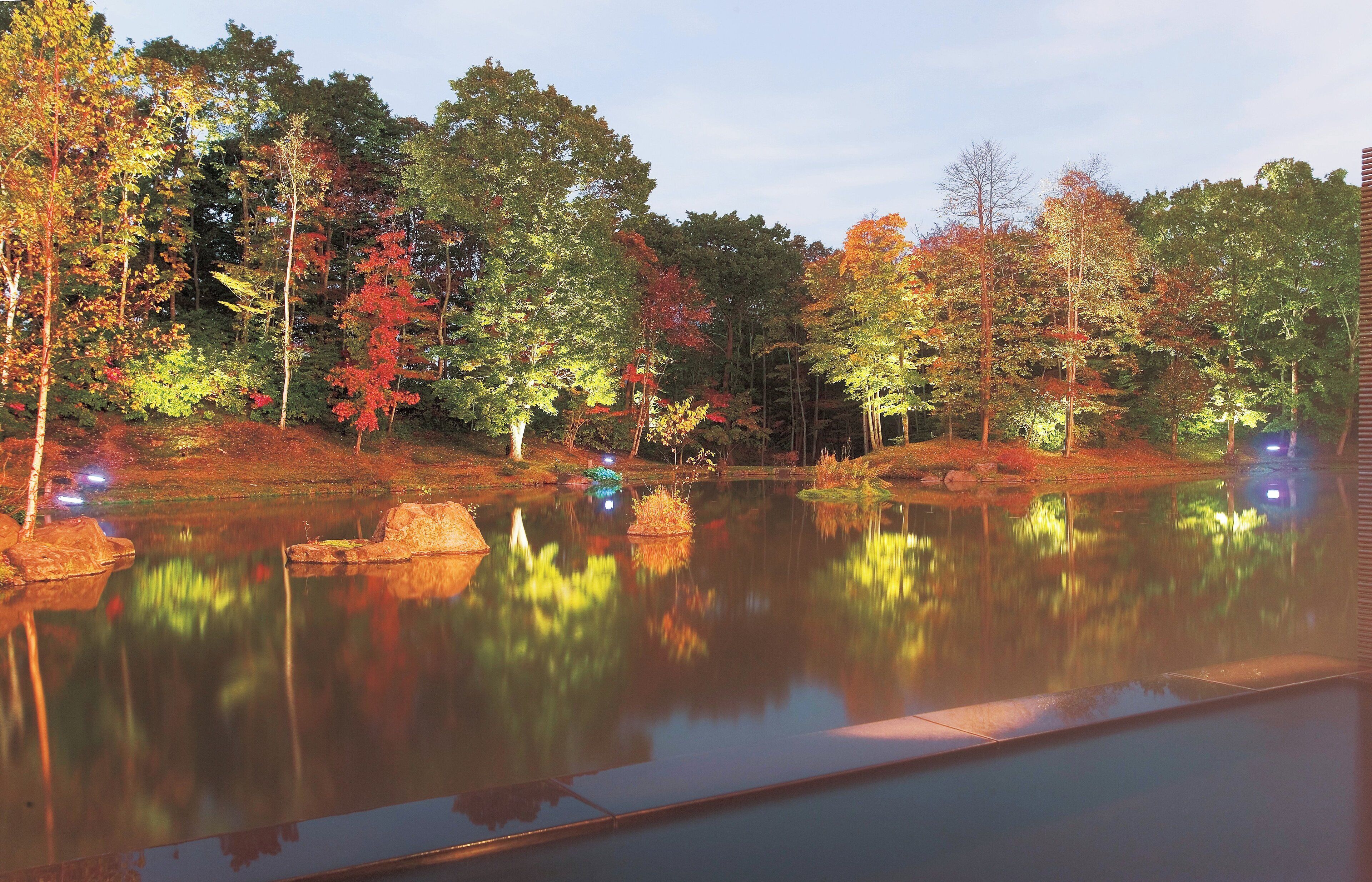 A tranquil outdoor scene with a reflective pond surrounded by trees with autumn foliage.