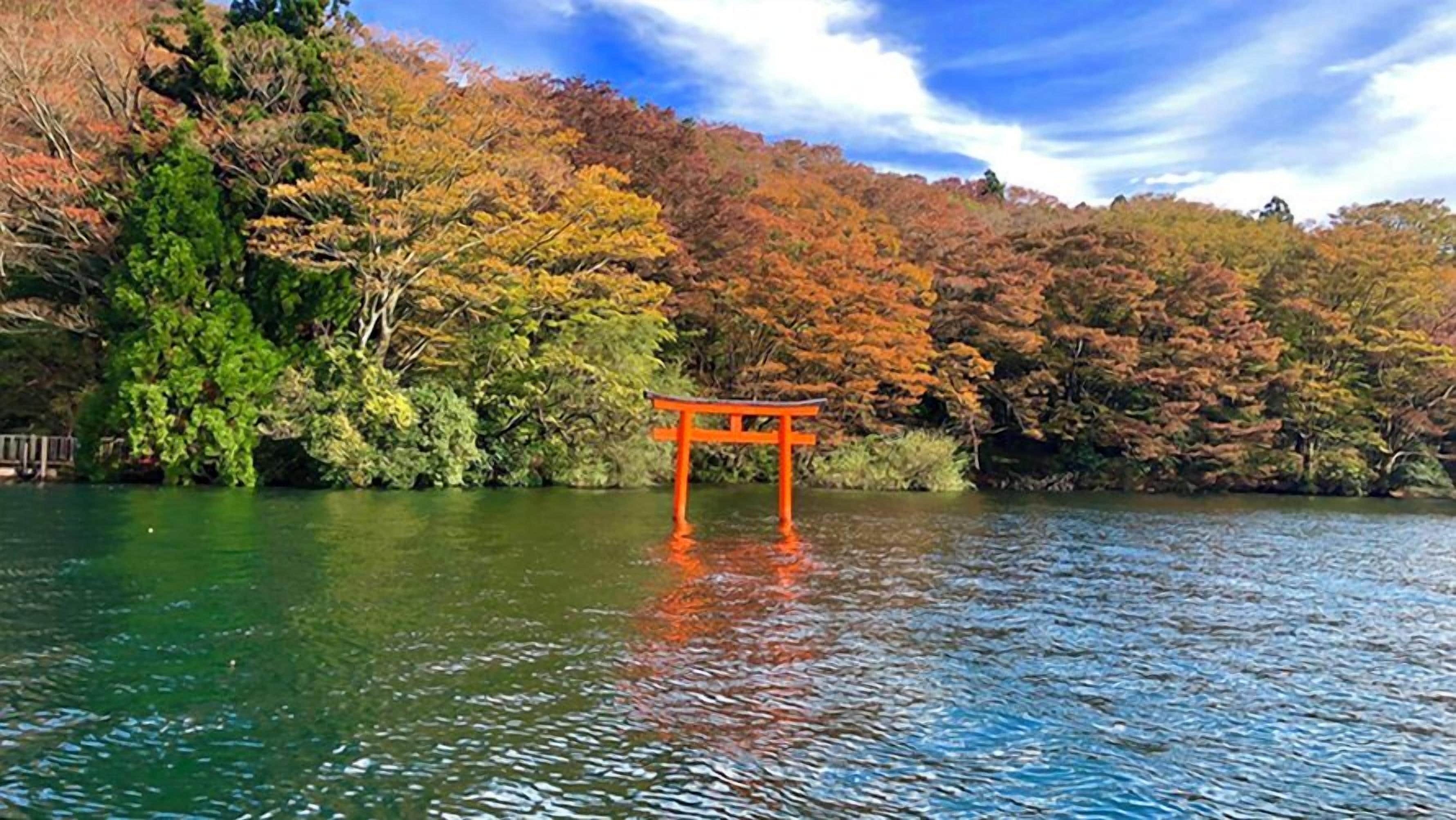 A traditional Japanese torii gate in a serene lake setting with autumn foliage.