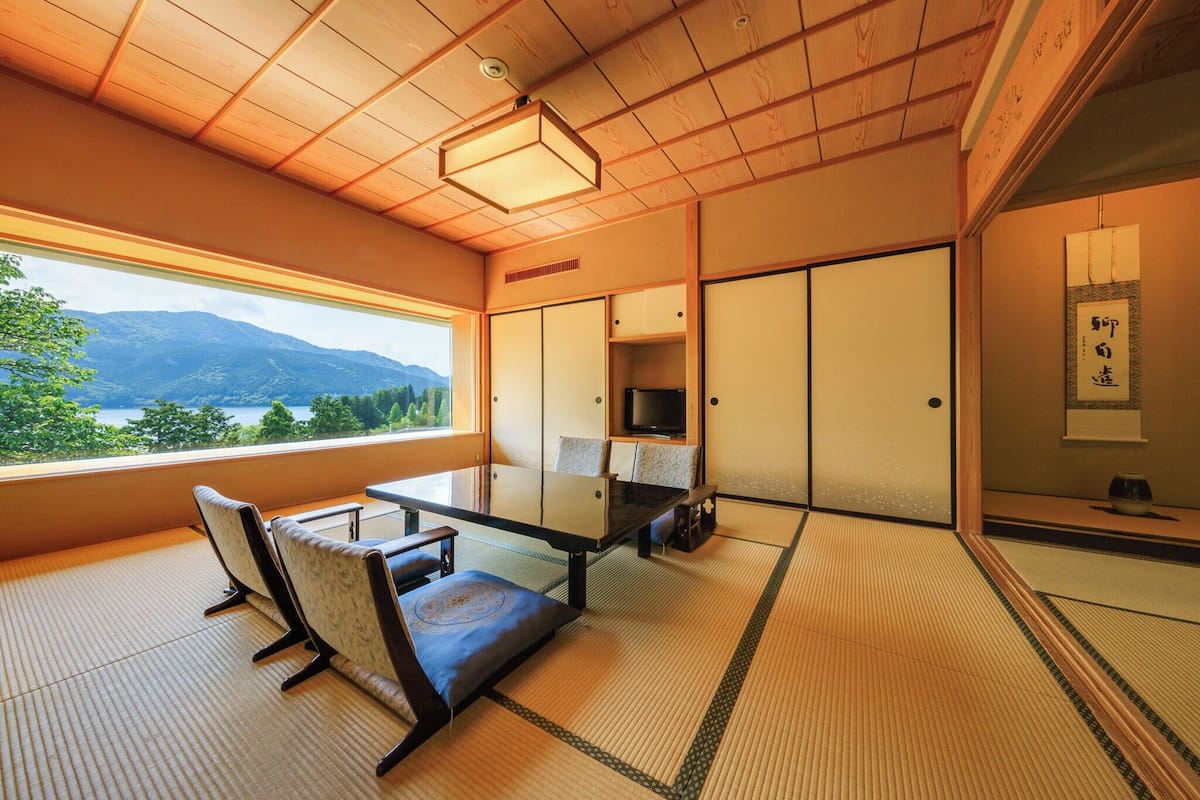 A traditional Japanese room with tatami flooring, a low table, and a view of mountains through a large window.