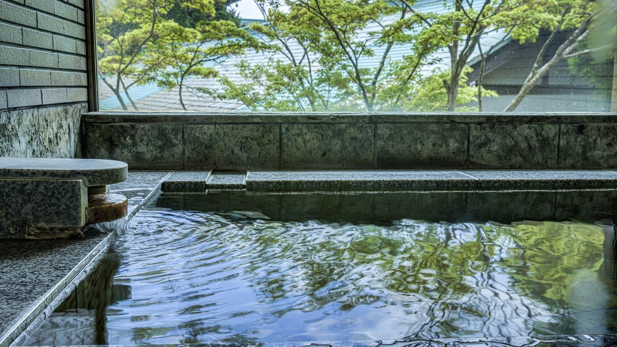 A stone hot spring with a view of trees and a building in the background.