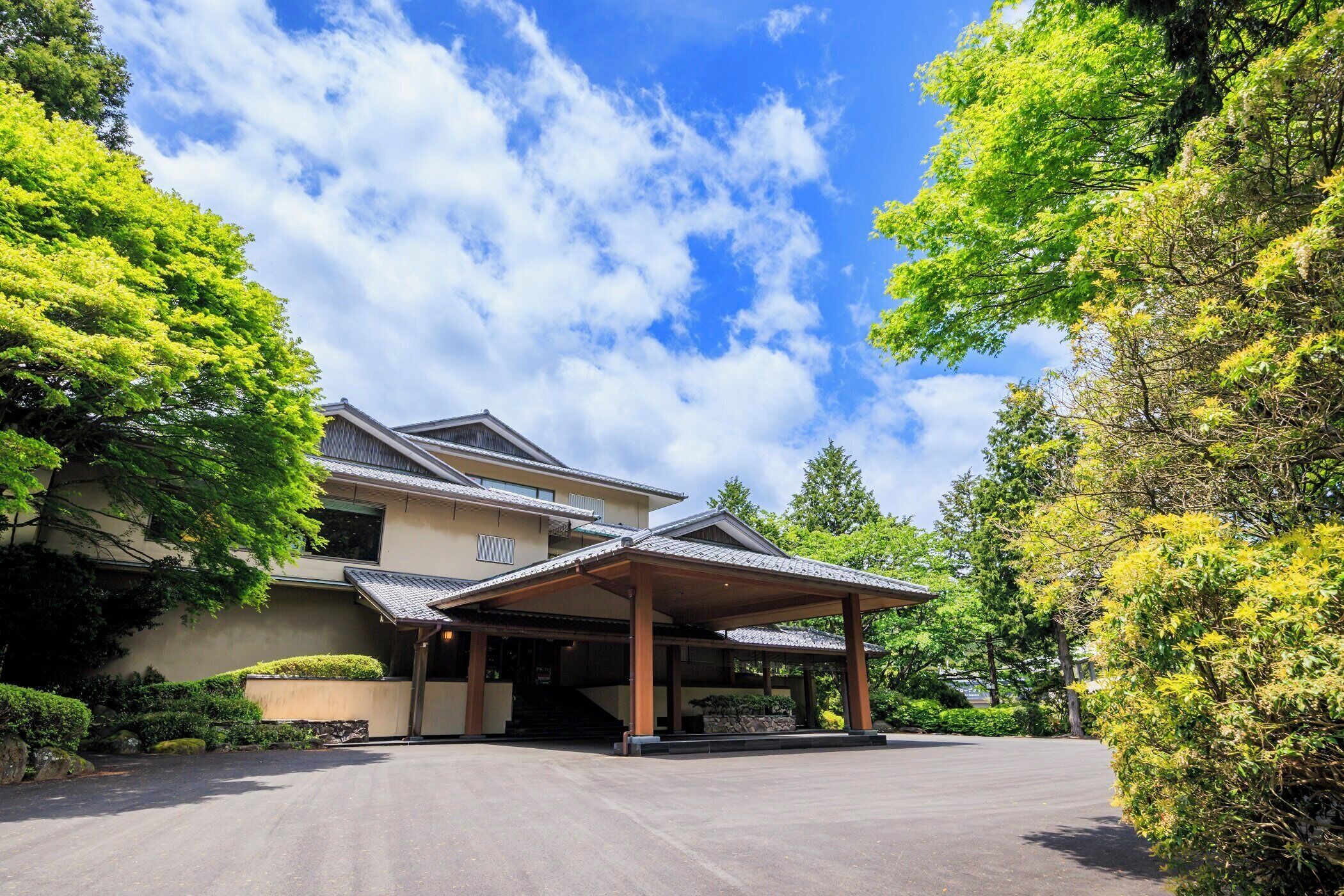 Een traditionele Japanse woning met een overdekte ingang, omringd door weelderige begroeiing en een heldere lucht.