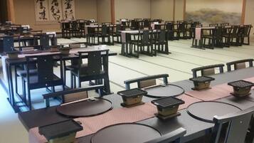 A room with multiple tables and chairs, arranged in rows. There are large calligraphy artworks on the walls.
