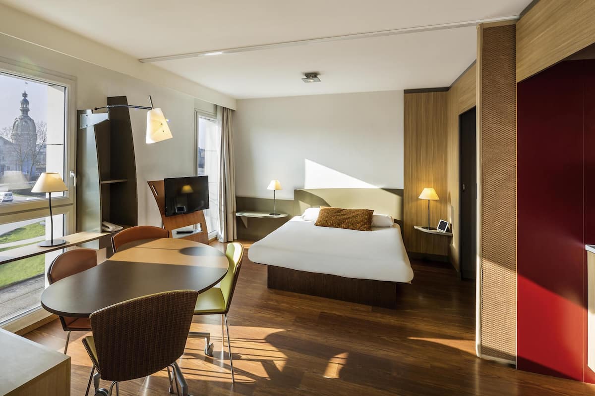 Une chambre d’hôtel équipée d’un lit, d’un bureau, d’une chaise, d’une table, d’une télévision et d’une fenêtre donnant sur un paysage agréable.