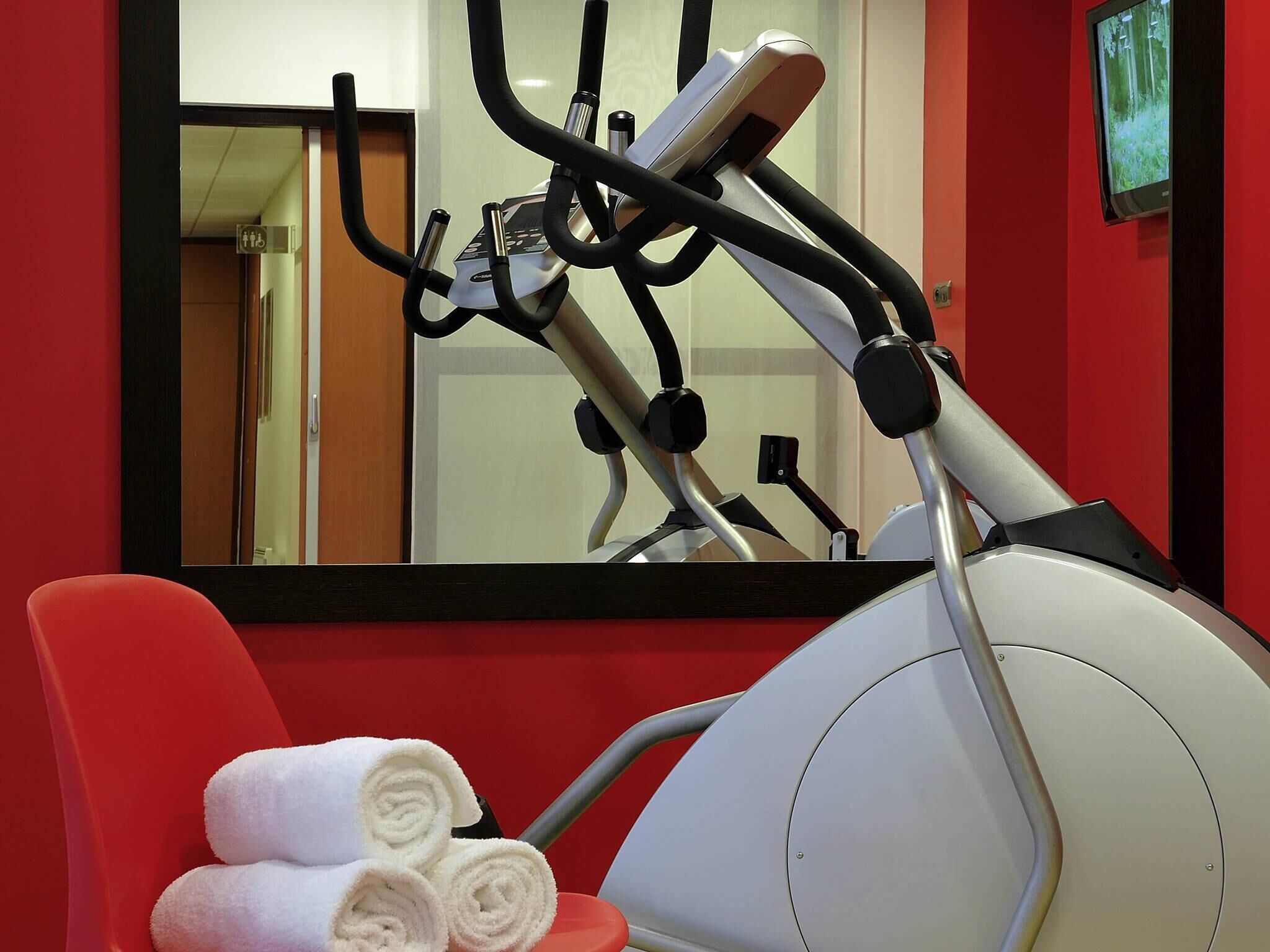 Un vélo d’appartement avec un miroir, un mur rouge et une serviette sur une chaise.