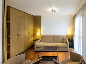 A modern living room with a sofa, two armchairs, a coffee table, a wardrobe, and two bedside tables with lamps.