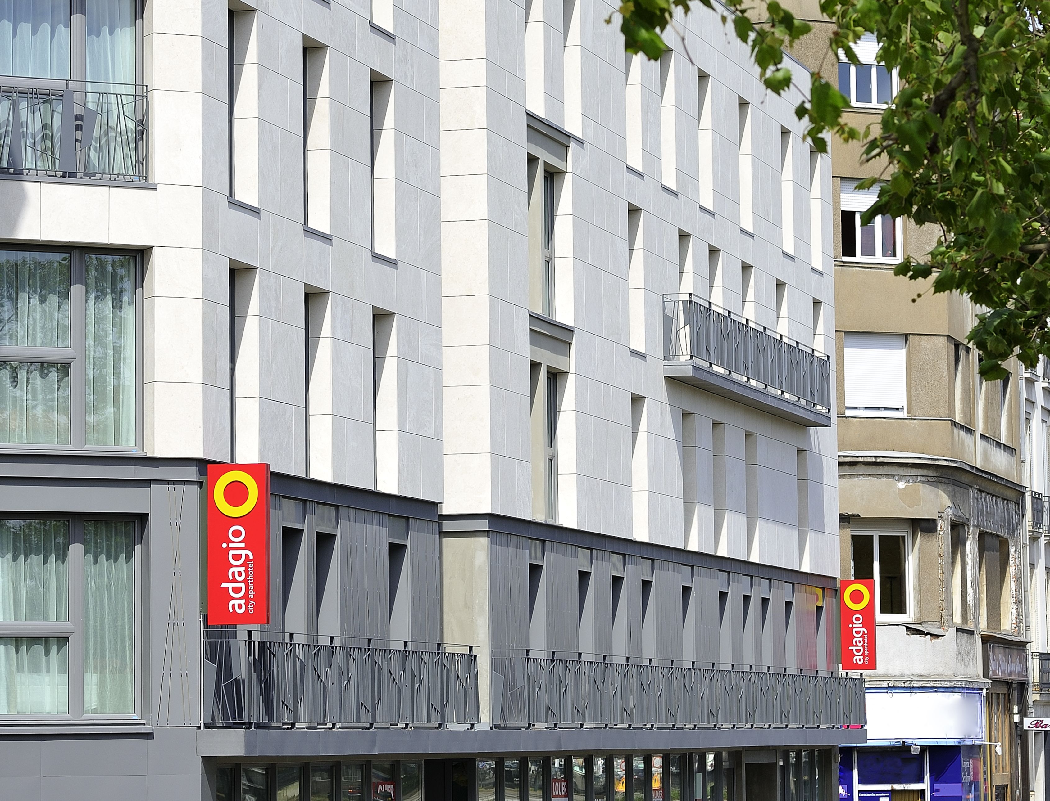 A modern building with a grid of windows and balconies. There are two red signs with the word "adagio" on them.