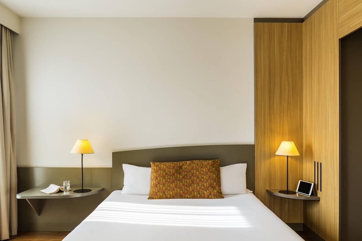Une chambre d’hôtel avec un grand lit, deux tables de chevet avec des lampes, un mur décoratif en bois et un petit bureau avec un ordinateur portable.