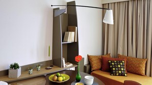 A modern hotel room with a dining table, a sofa, a bookshelf, and a lamp.