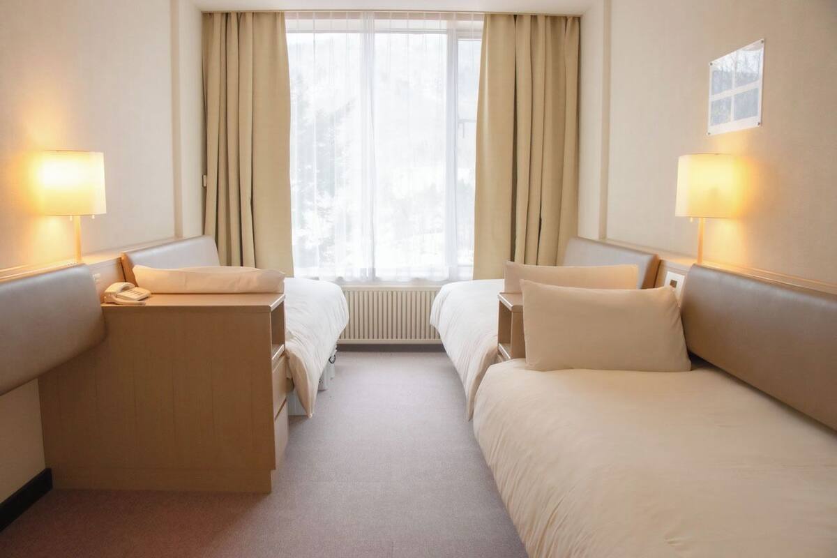 Habitación de hotel con dos camas, un escritorio y una ventana con cortinas.