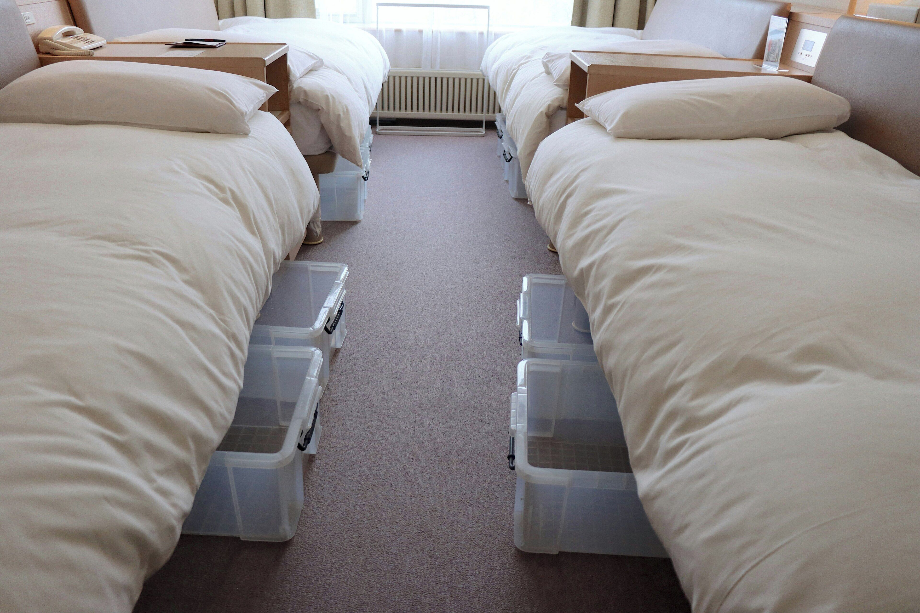 Ein Hotelzimmer mit zwei Betten, einem Nachttischtelefon, einer Heizung und Staufächern unter den Betten.